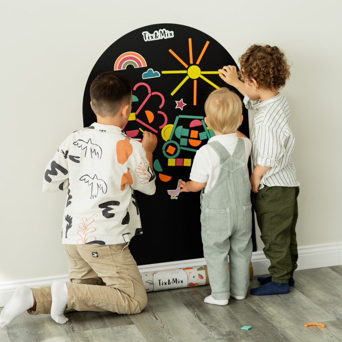 Three children playing with Tix & Mix wooden magnets on a magnetic wall decal.