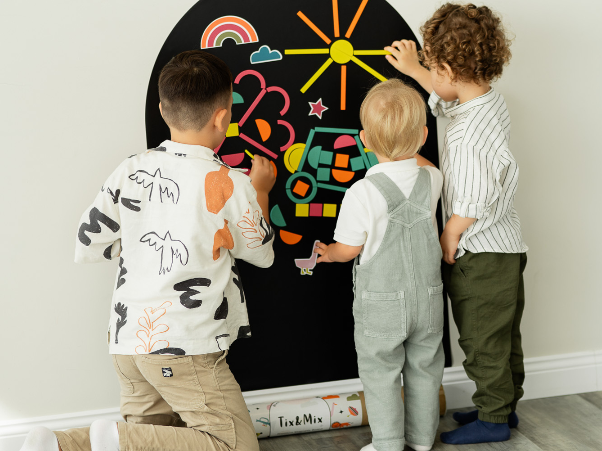 Three children playing with Tix & Mix wooden magnets on a magnetic wall decal.
