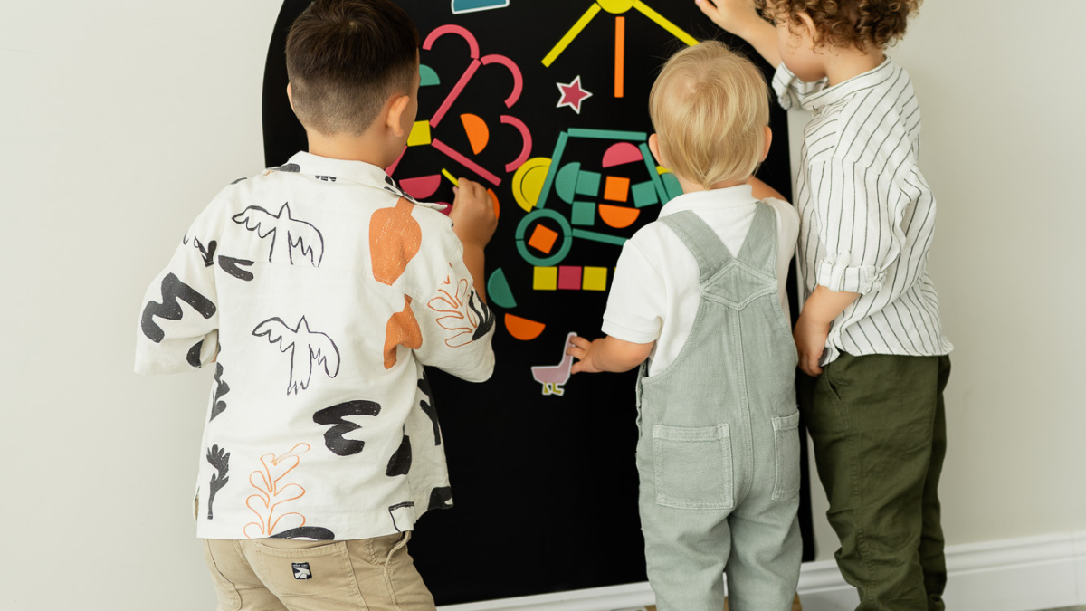 Three children playing with Tix & Mix wooden magnets on a magnetic wall decal.