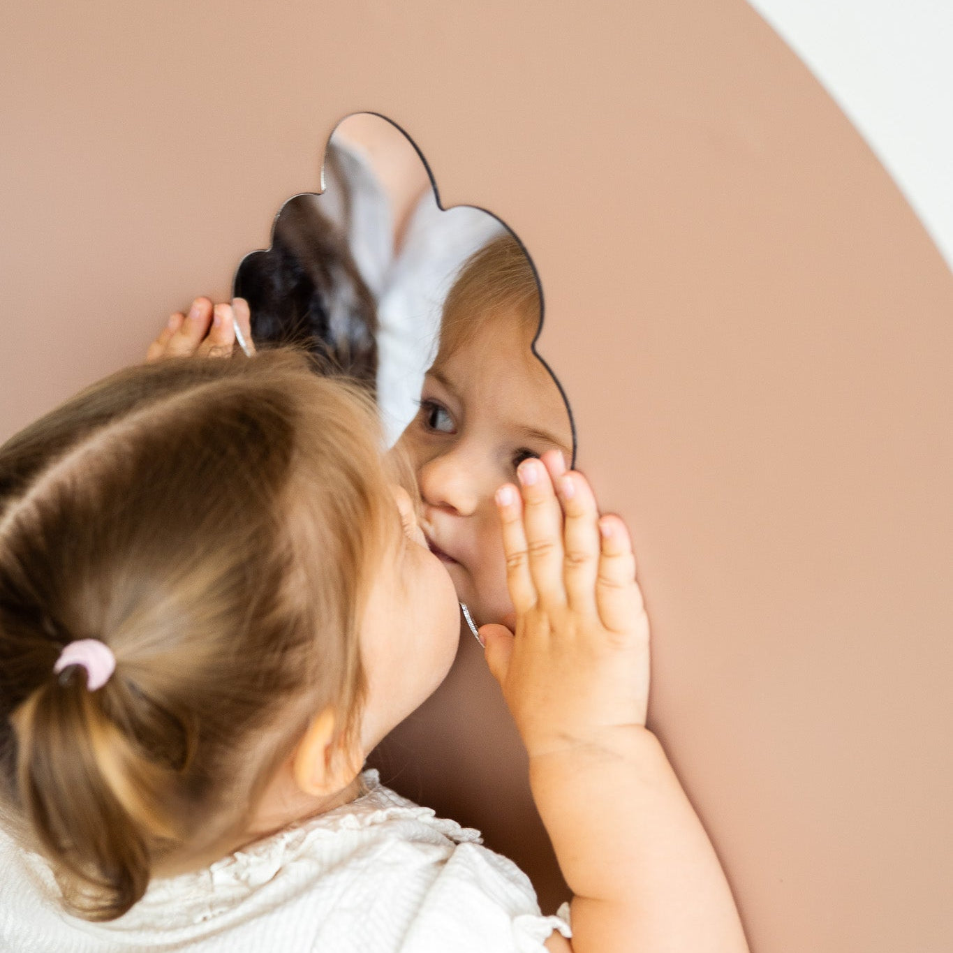 A kid looking at herself on a magnetic mirror placed on a magnetic wall board.