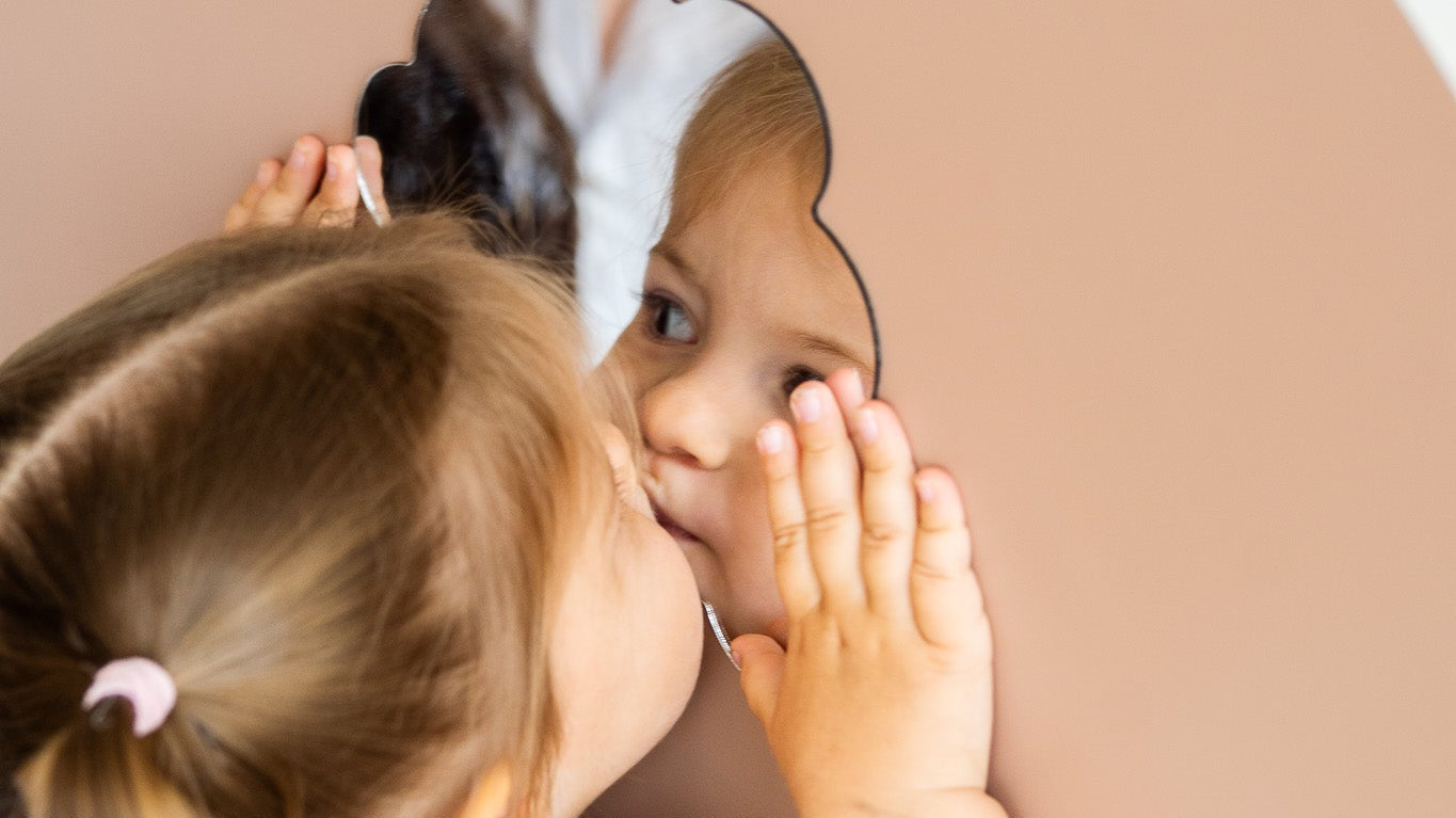 A kid looking at herself on a magnetic mirror placed on a magnetic wall board.