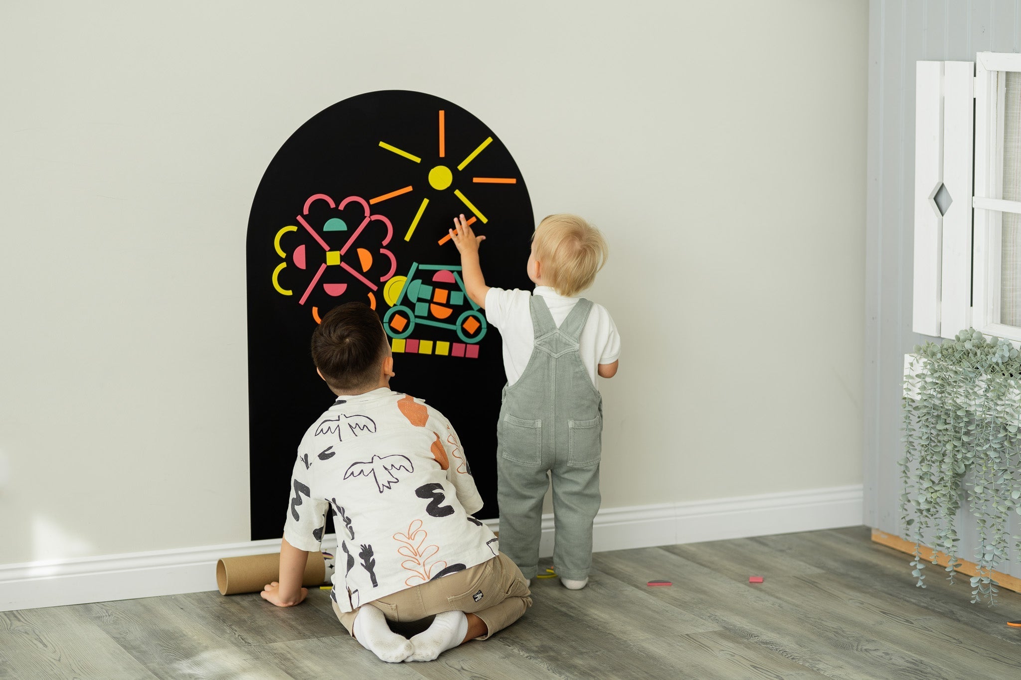 Two kids playing with Tix&Mix magnetic wall board and magnetic toys.