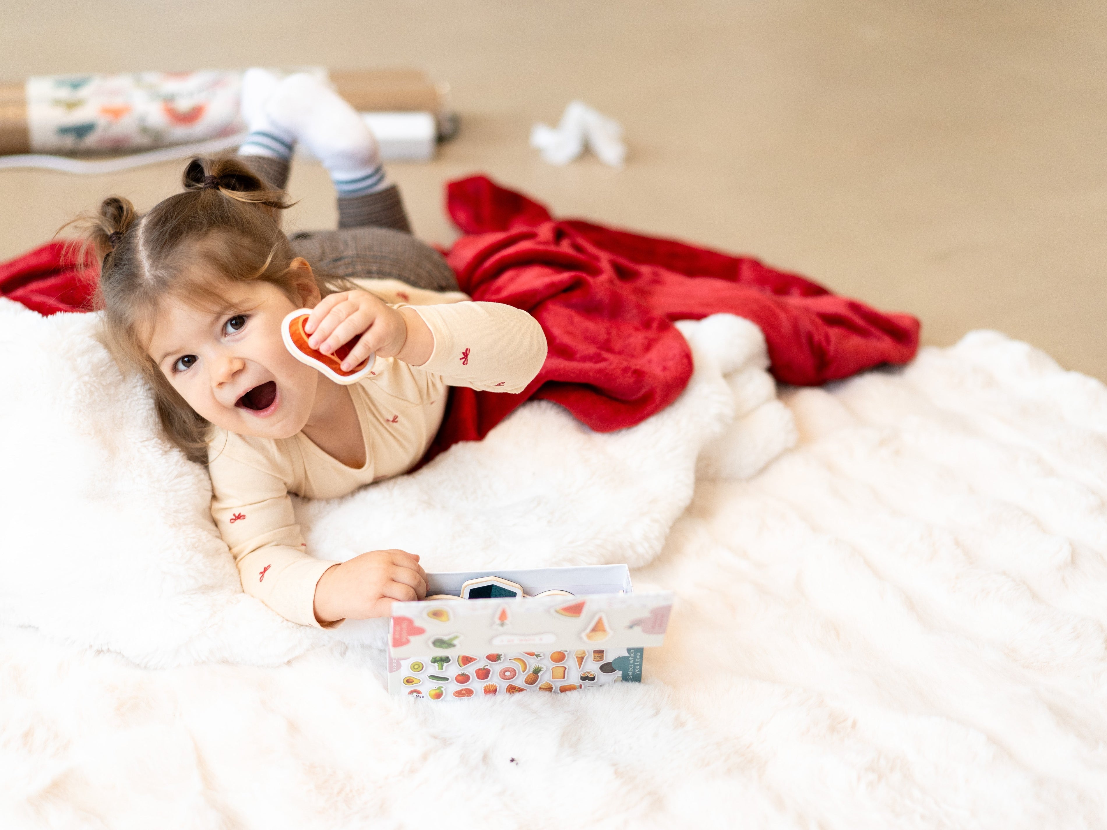 A toddler laying on a white rug while holding Tix&Mix magnetic play sets.