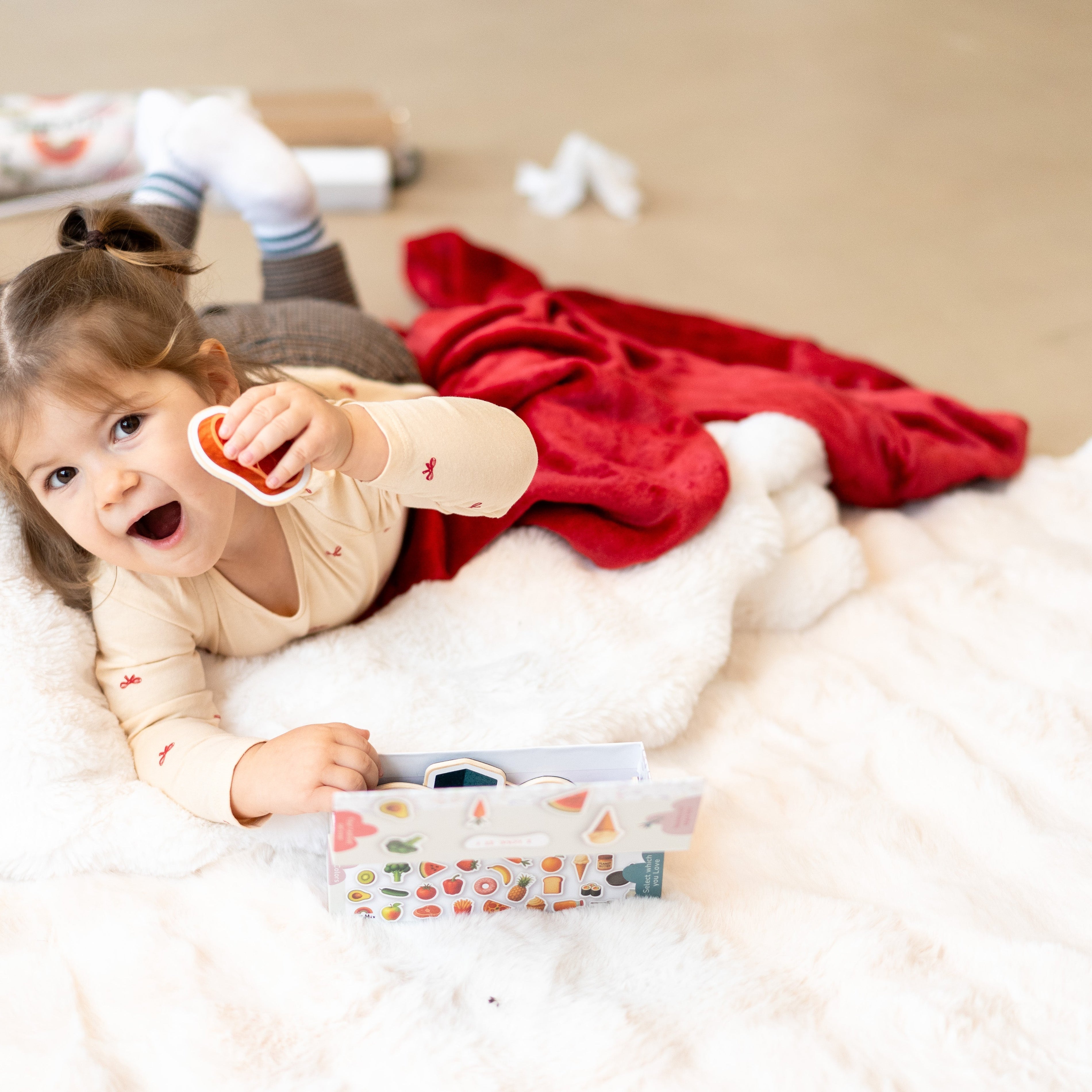 A toddler laying on a white rug while holding Tix&Mix magnetic play sets.