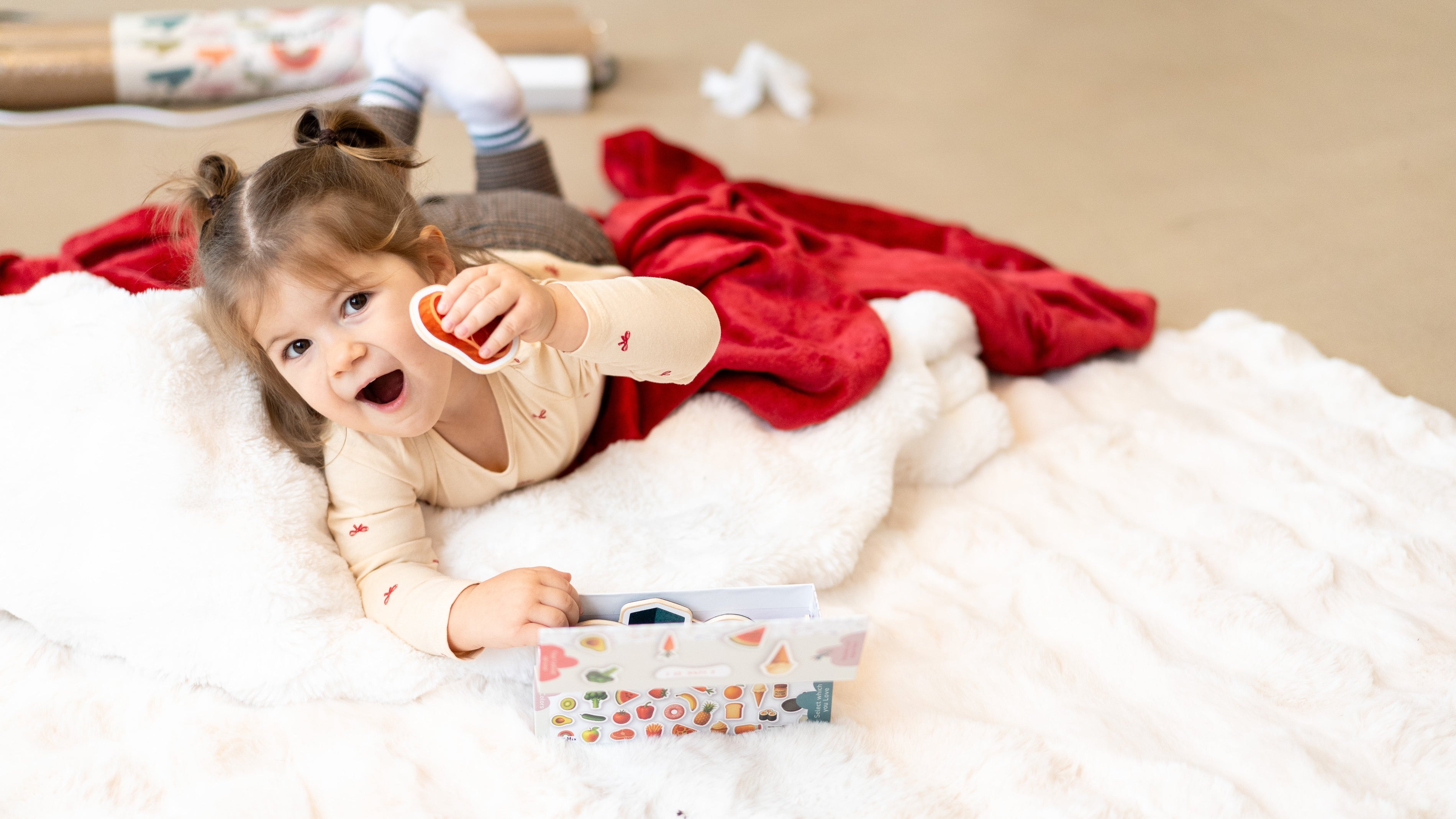 A toddler laying on a white rug while holding Tix&Mix magnetic play sets.