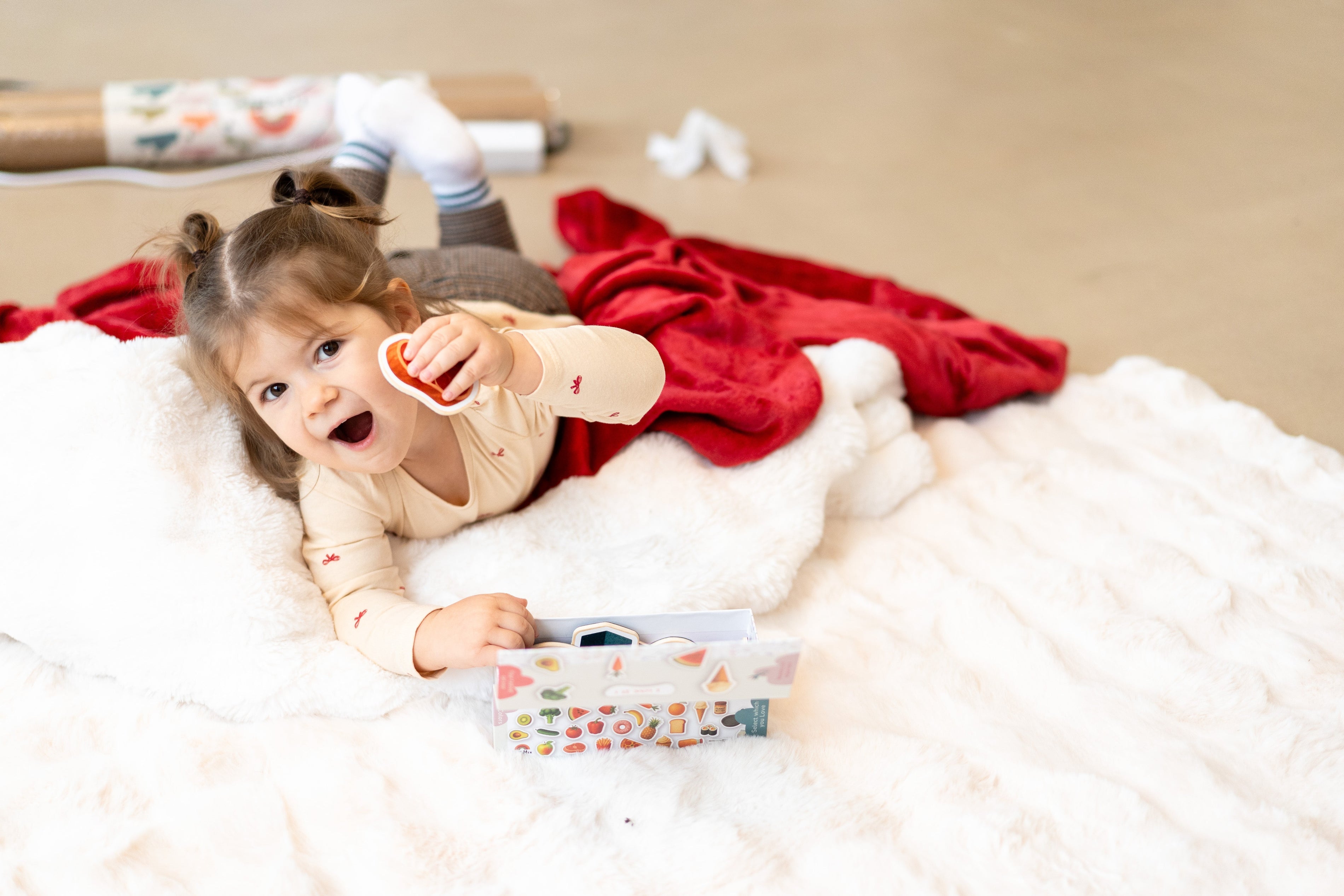 A toddler laying on a white rug while holding Tix&Mix magnetic play sets.