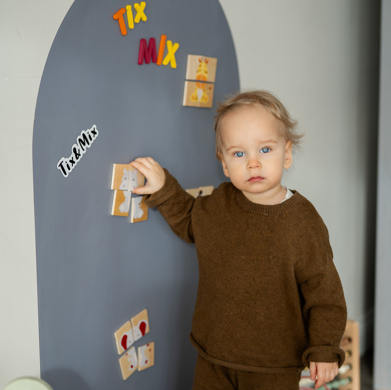 A toddler playing with wooden magnets on a Tix & Mix magnetic wall board that encourages creative play and early learning.