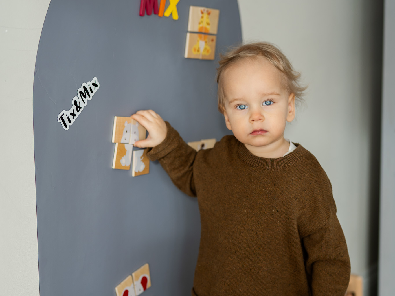 A toddler playing with wooden magnets on a Tix & Mix magnetic wall board that encourages creative play and early learning.