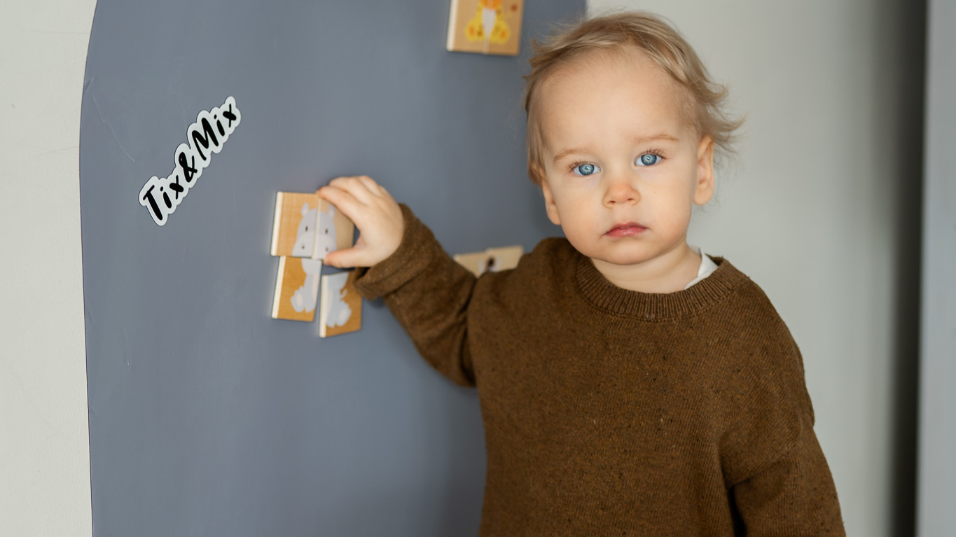 A toddler playing with wooden magnets on a Tix & Mix magnetic wall board that encourages creative play and early learning.