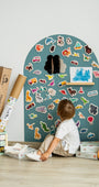 A toddler looking at the magnetic animal toys attached on a cyan wave magnetic wall decal.