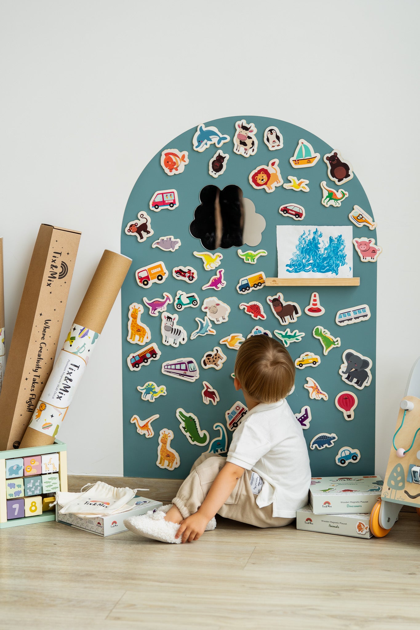 A toddler looking at the magnetic animal toys attached on a cyan wave magnetic wall decal.