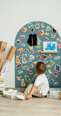 A kid sitting in front of Tix&Mix cyan wave magnetic wall decal featuring animals and vehicles wooden toys.