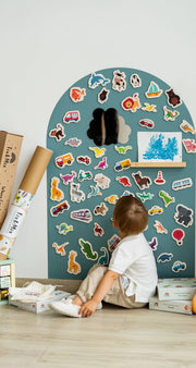 A kid sitting in front of Tix&Mix cyan wave magnetic wall decal featuring animals and vehicles wooden toys.