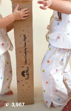 Two children standing next to a tall cardboard box with text on it, against a plain background.