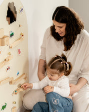 A kid playing with Tix&Mix magnetic toys on a white magnetic wall decal assisted by her parent.