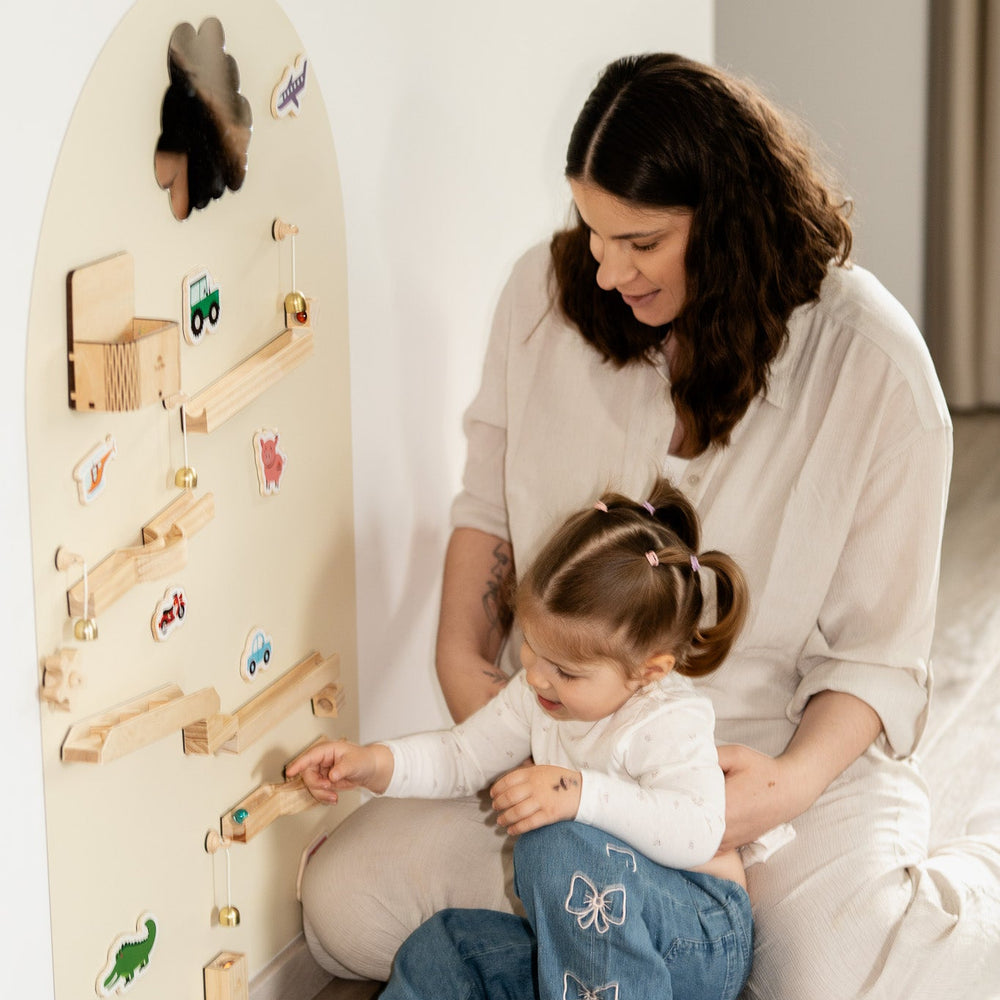 A kid playing with Tix&Mix magnetic toys on a white magnetic wall decal assisted by her parent.