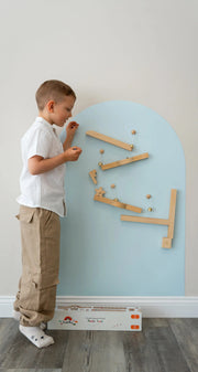 A male kid playing with Tix&Mix marble track on a blue magnetic wall decal.