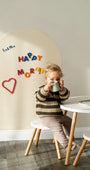 A kid sitting on a chair featuring a white wall decal on the background with Happy Morning text.