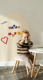 A kid sitting on a chair featuring a white wall decal on the background with Happy Morning text.