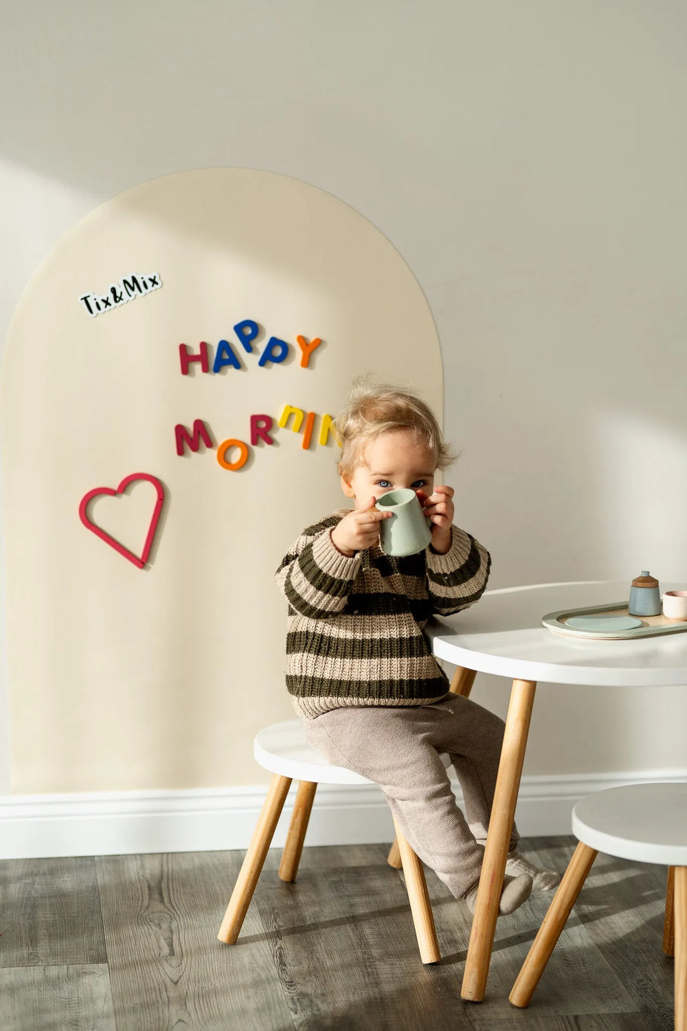 A kid sitting on a chair featuring a white wall decal on the background with Happy Morning text.