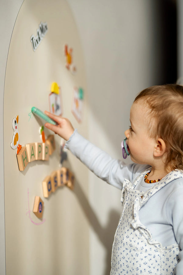 A toddler using a Tix&Mix crayon on a white magnetic wall decal.