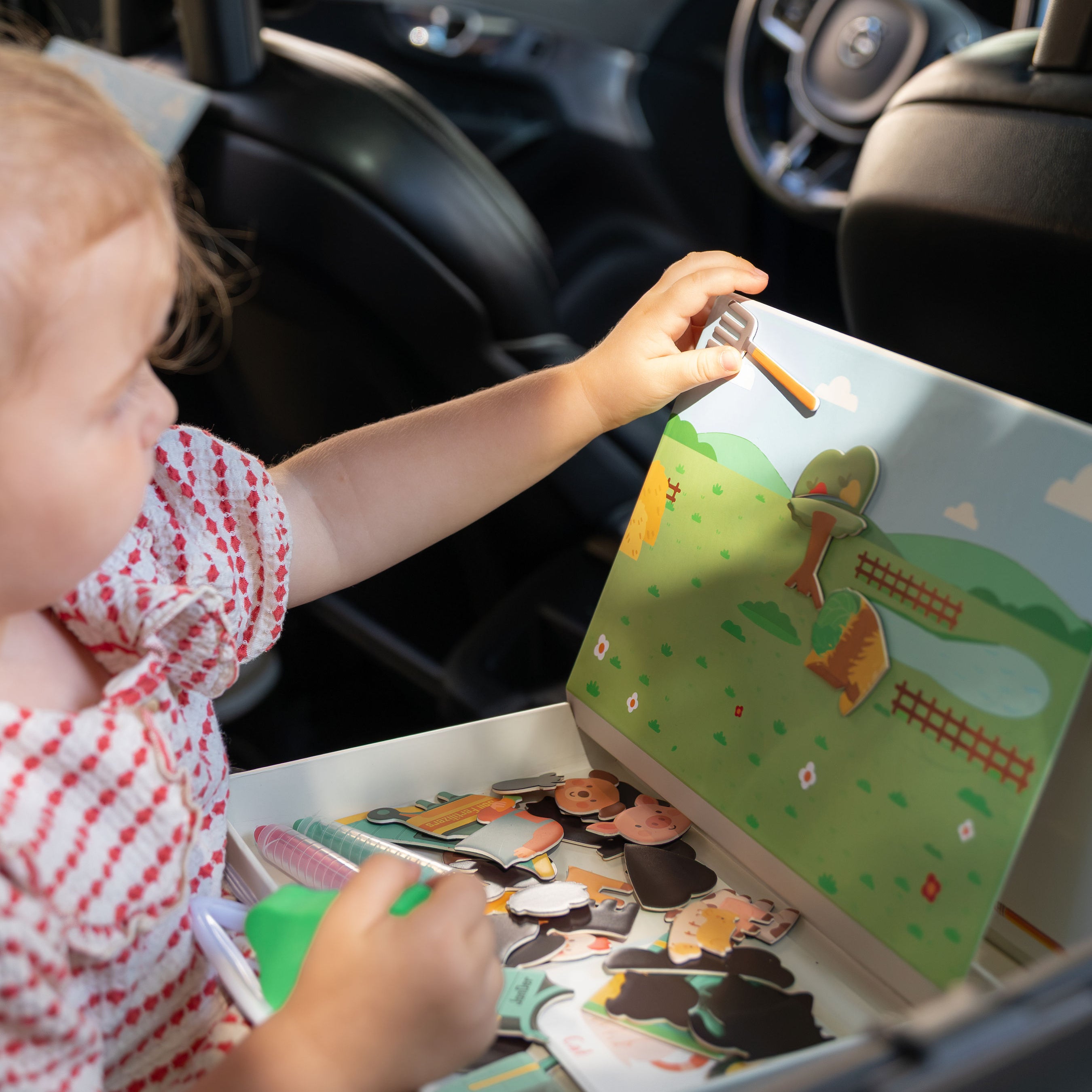 A female kid playing with Tix&Mix magnetic play box Farm Zone inside a car.