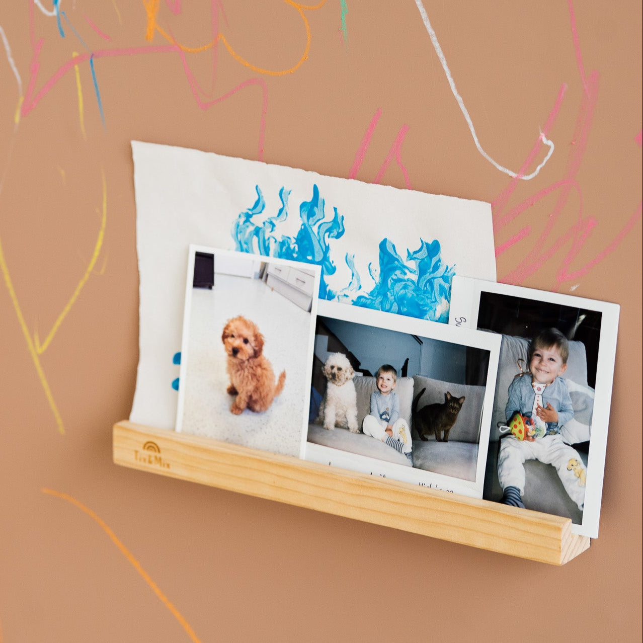 Wooden photo ledge with photos on a brown wall with colorful scribbles