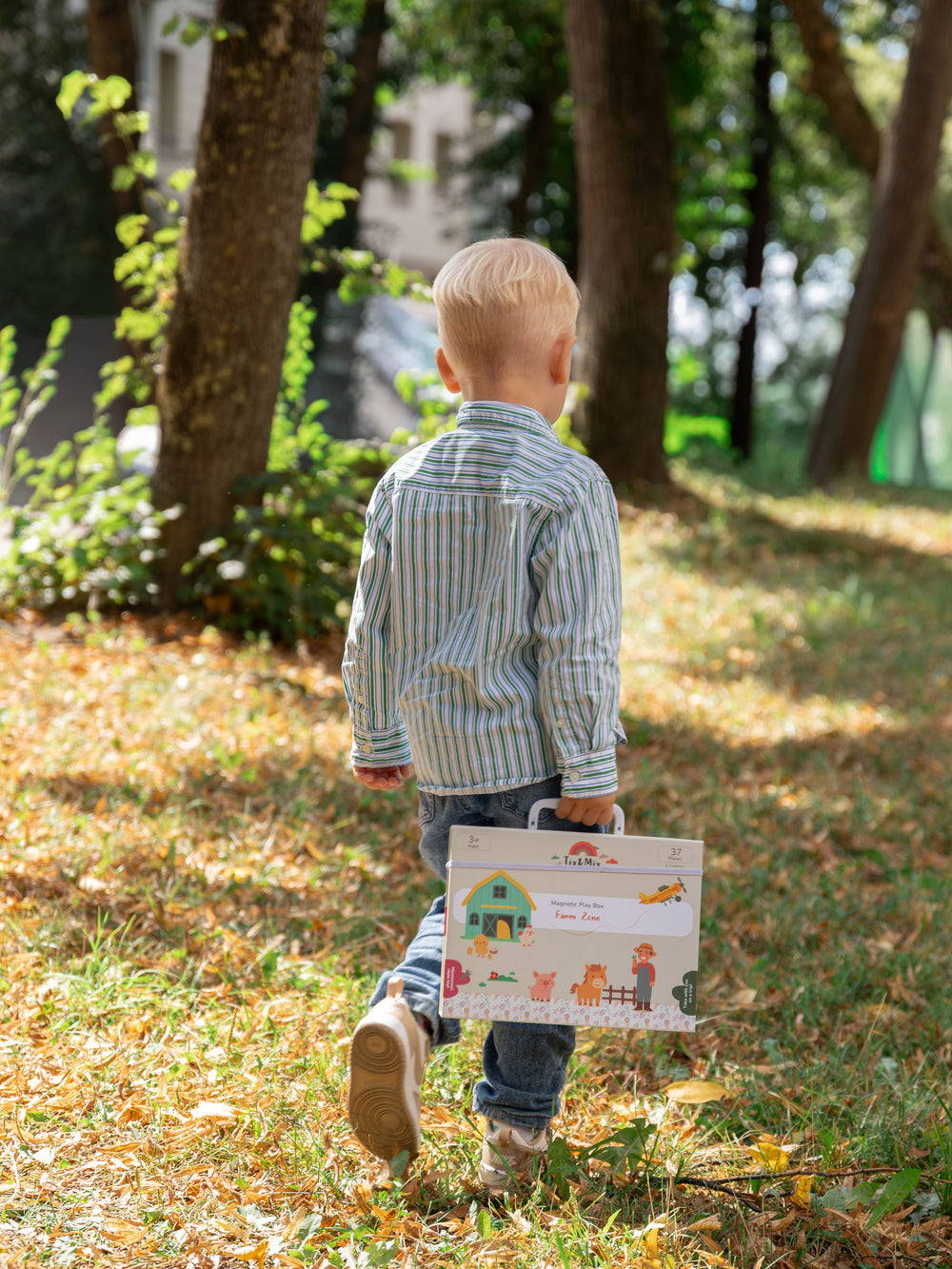 A male kid walking outside while holding the Tix&Mix magnetic play box magnetic farm zone set.