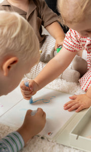 Three kids learning how to draw on a white clear paper using the Tix&Mix colorful crayons.