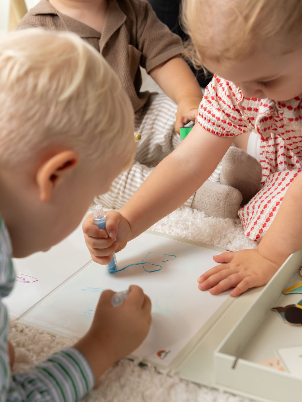 Three kids learning how to draw on a white clear paper using the Tix&Mix colorful crayons.