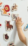 A hand of a toddler playing with Tix&Mix magnetic animals toys on a white magnetic wall decal.