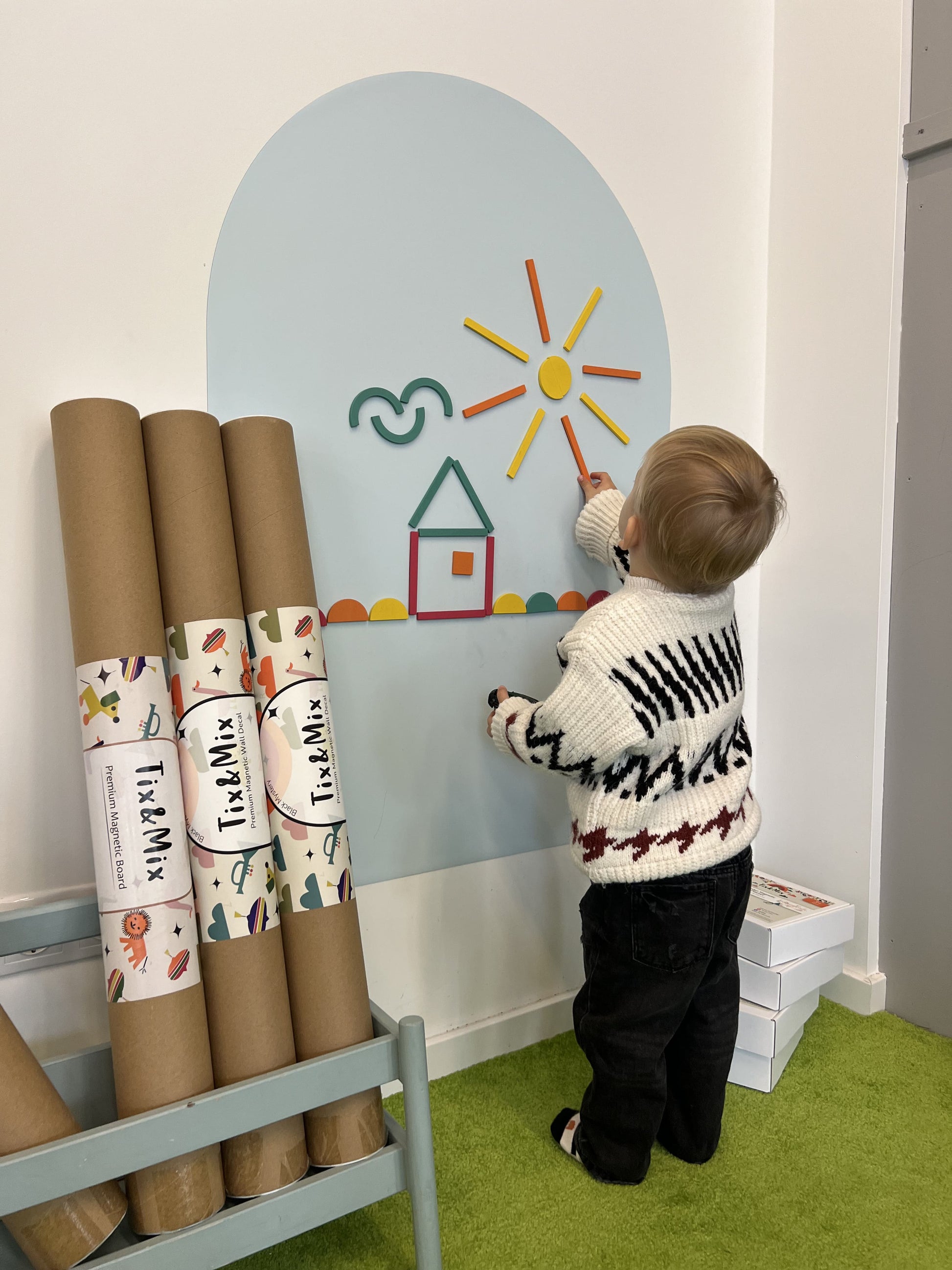 A toddler playing with Tix&Mix Rings and Blocks Play Kit on a Blue Dream magnetic wall decal.