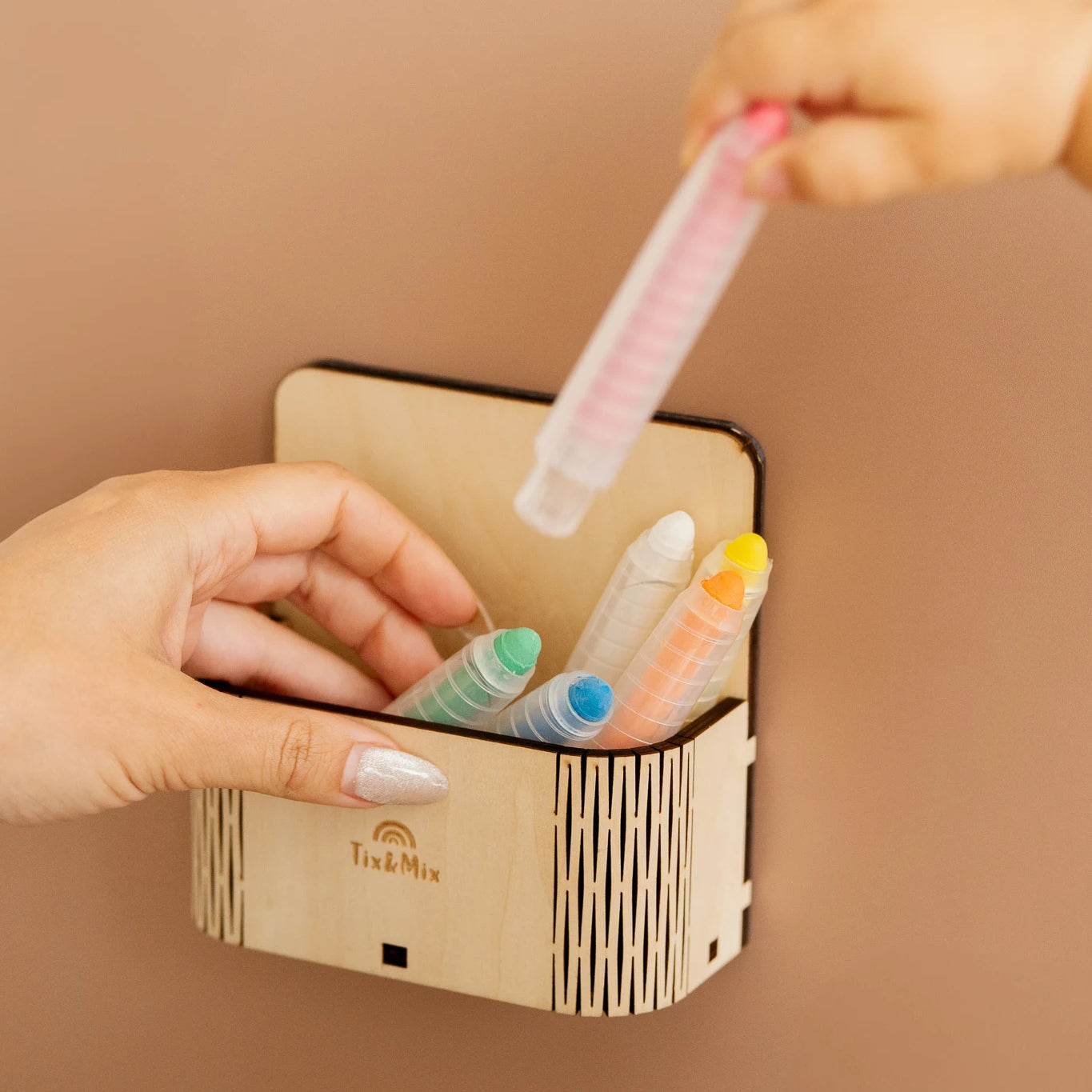 A toddlers hand placing a crayon on a magic box attached to a brown magnetic wall decal.