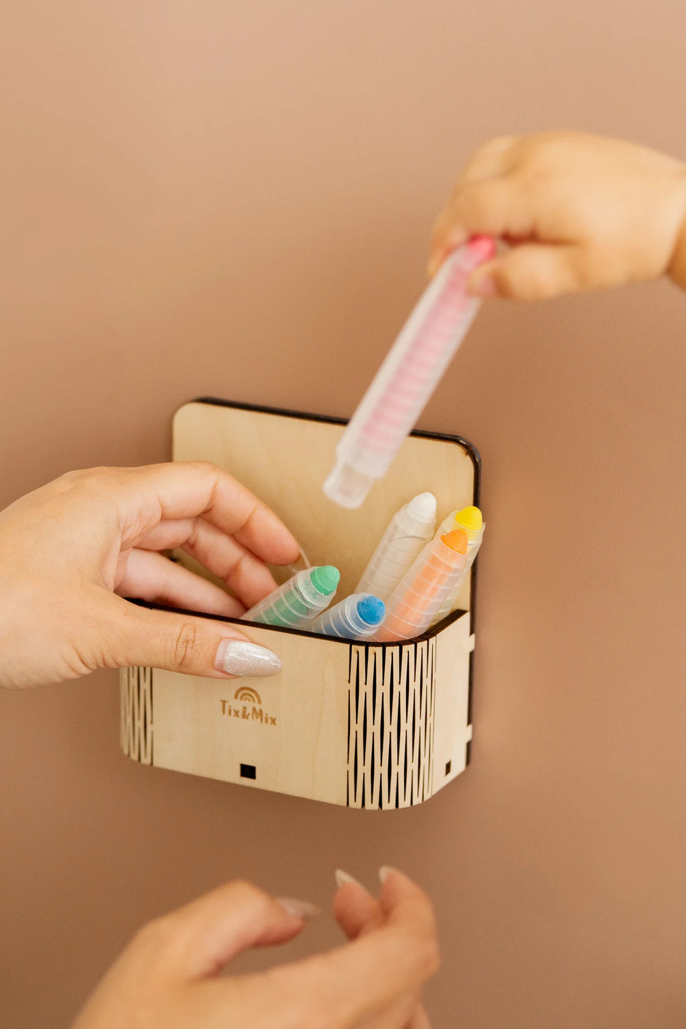 A toddlers hand placing a crayon on a magic box attached to a brown magnetic wall decal.
