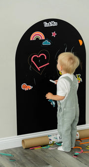 A toddler drawing on a black magnetic wall decal using Tix&Mix crayon.