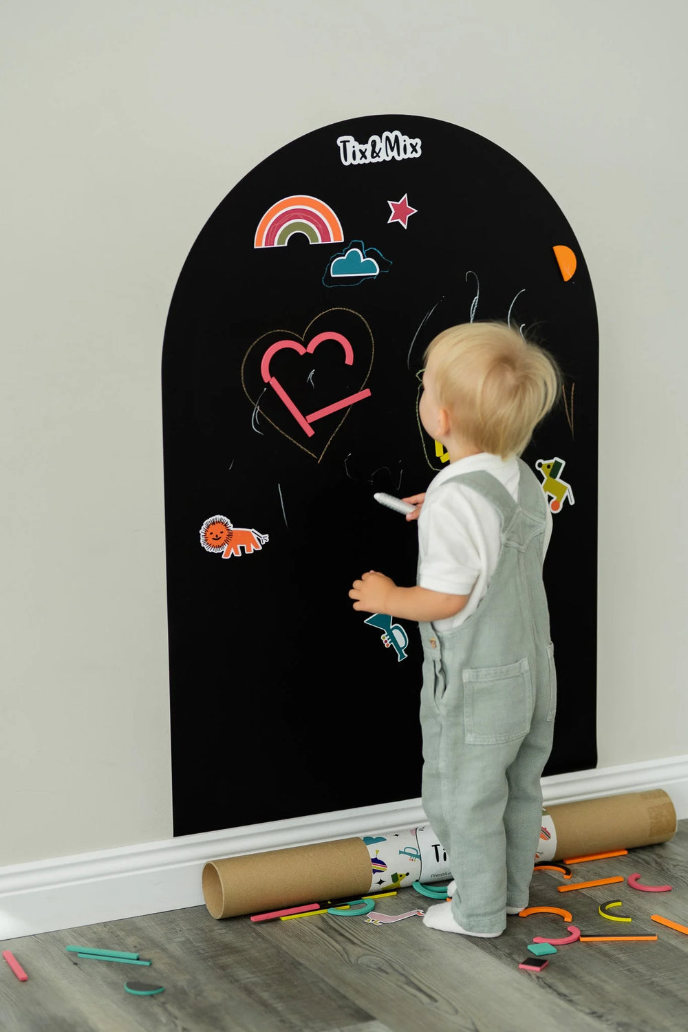 A toddler drawing on a black magnetic wall decal using Tix&Mix crayon.
