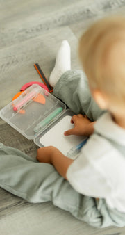 A toddler sitting on the floor while holding the Tix&Mix crayon case.