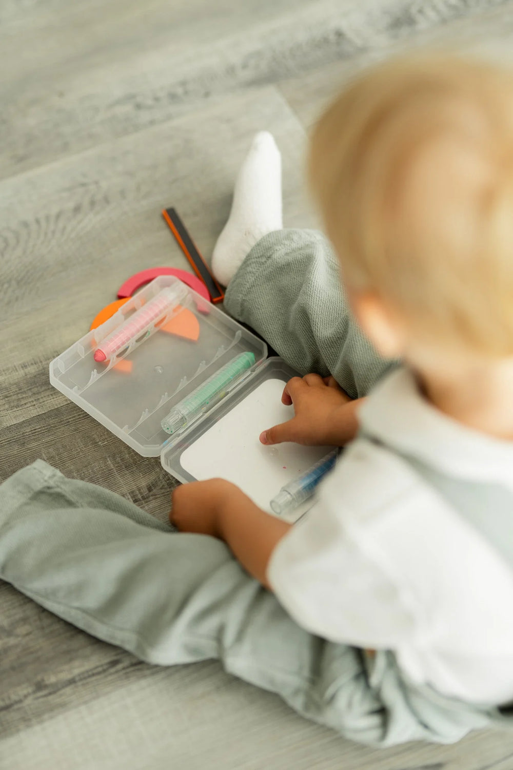 A toddler sitting on the floor while holding the Tix&Mix crayon case.