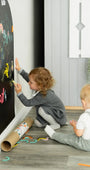Two toddlers drawing on a black magnetic wall decal using Tix&Mix colorful crayons.