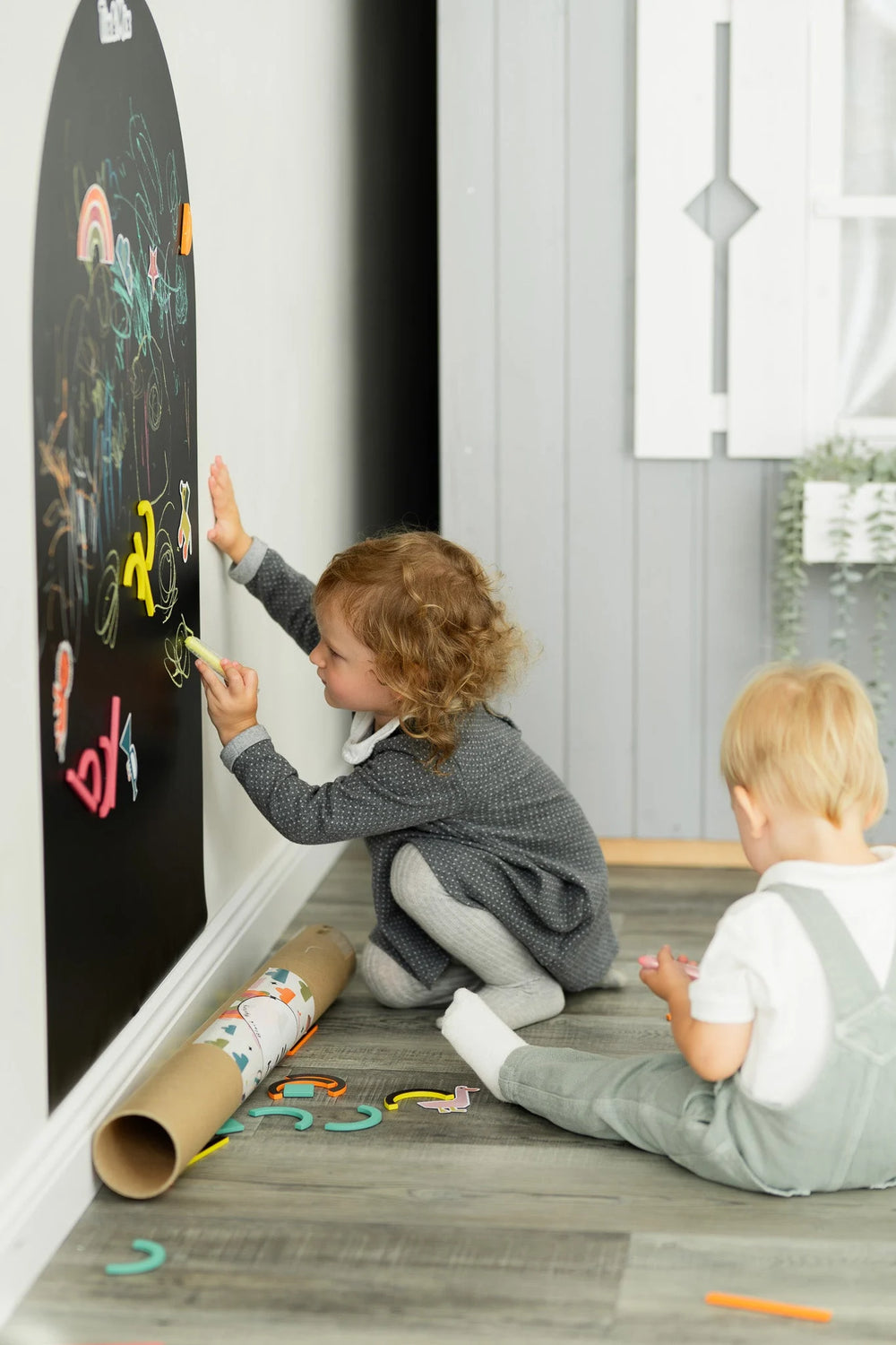 Two toddlers drawing on a black magnetic wall decal using Tix&Mix colorful crayons.