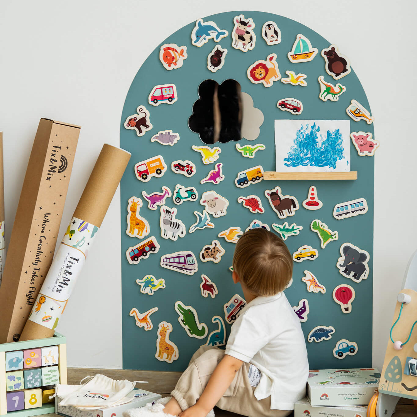 A male toddler looking up at the Tix&Mix cyan magnetic wall decal with magnetic toys placed on it.