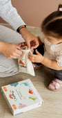 A toddler assisting a parent holding a white Tix&Mix white bag with Dinosaur packaging box on the floor.