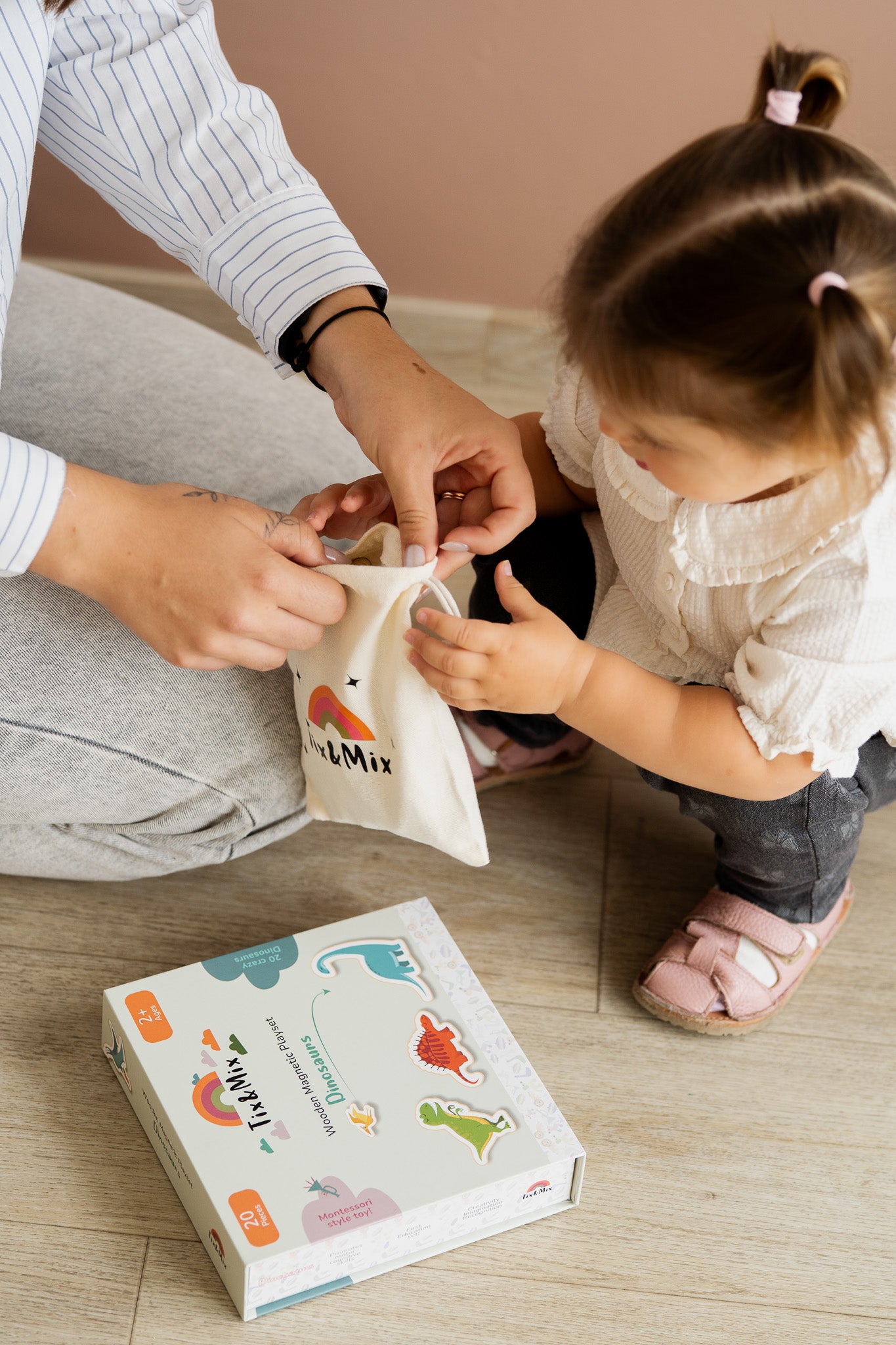 A toddler assisting a parent holding a white Tix&Mix white bag with Dinosaur packaging box on the floor.