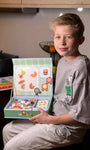A male kid sitting and looking at the camera while holding Tix&Mix Food discovery set for kids.
