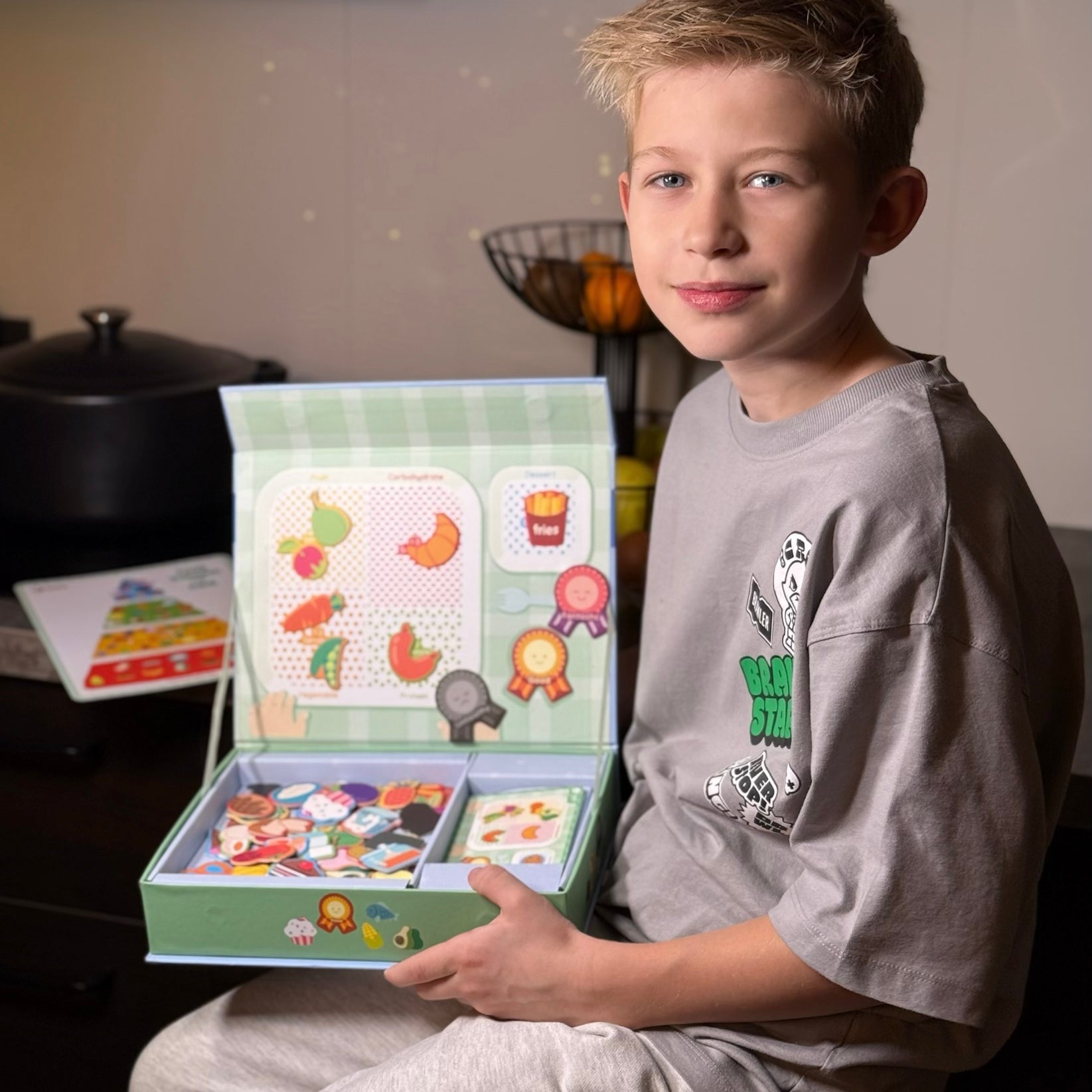A male kid sitting and looking at the camera while holding Tix&Mix Food discovery set for kids.