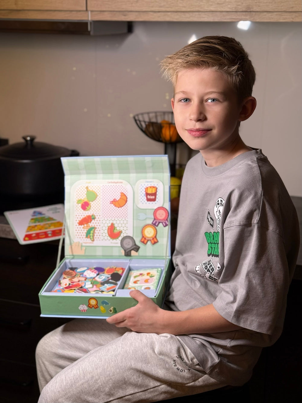 A male kid sitting and looking at the camera while holding Tix&Mix Food discovery set for kids.