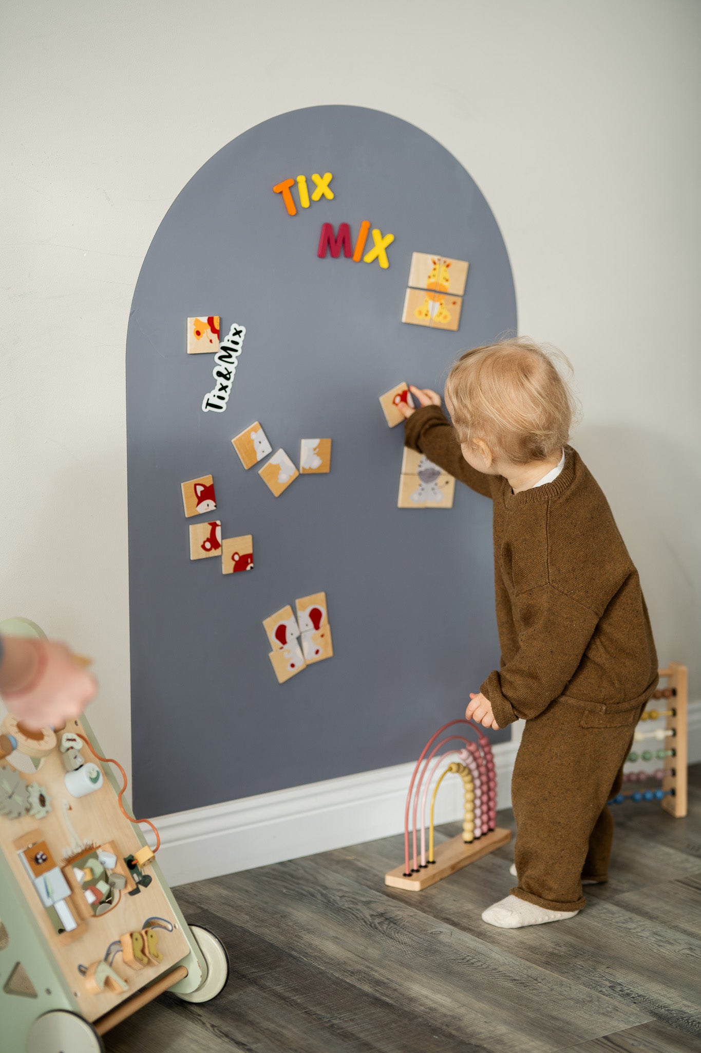 A toddler playing with TixMix magnetic animals puzzle play set on a grey wall decal.