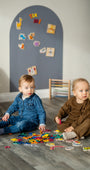 Two toddlers playing with Tix&Mix magnetic toys on a floor with grey wall decal on the background.