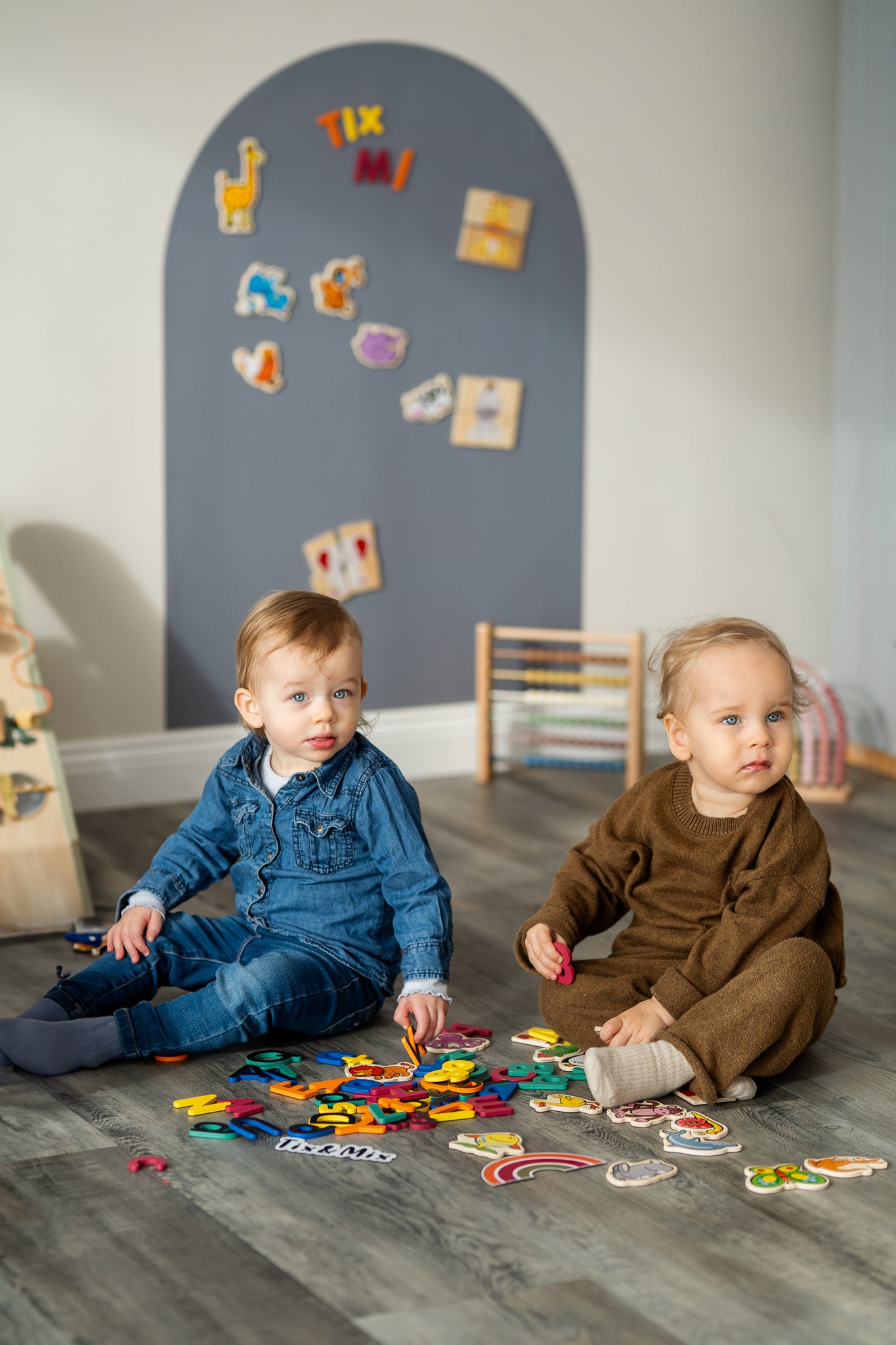 Two toddlers playing with Tix&Mix magnetic toys on a floor with grey wall decal on the background.