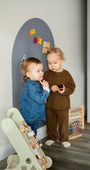 Two toddlers playing with Tix&Mix magnetic toys on a grey wall decal.